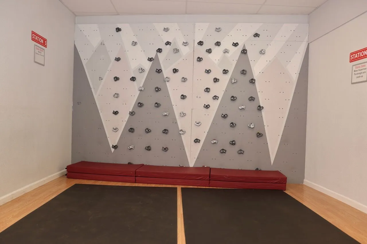 The studio climbing wall above a padded red bench