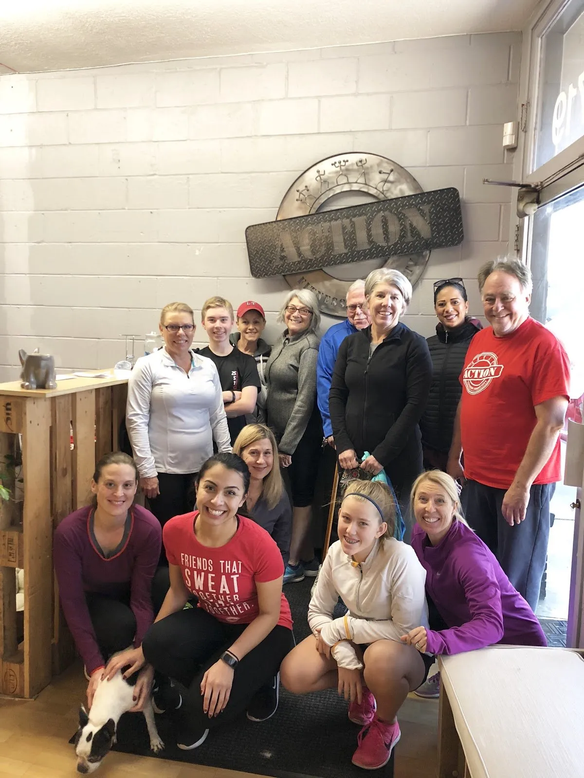 A group of smiling Action Fitness members gathered under the ACTION sign in the studio lounge