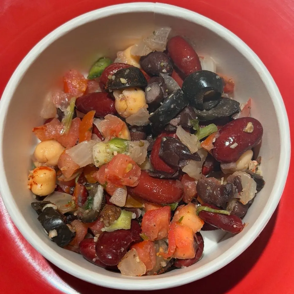 A bowl of The Get A Grip three bean salad with tomatoes and olives
