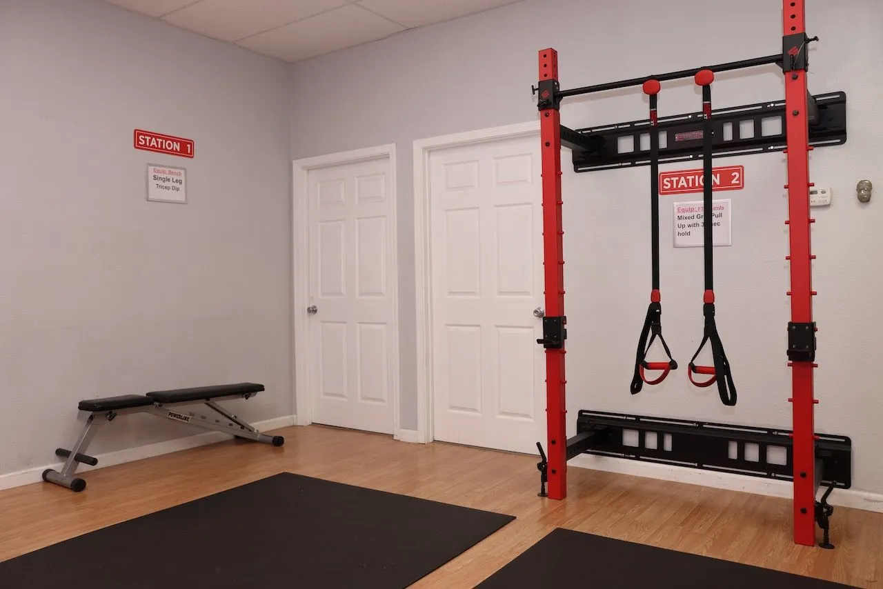 A red wall-mounted squat rack with Jungle Gym suspension straps above an adjustable bench