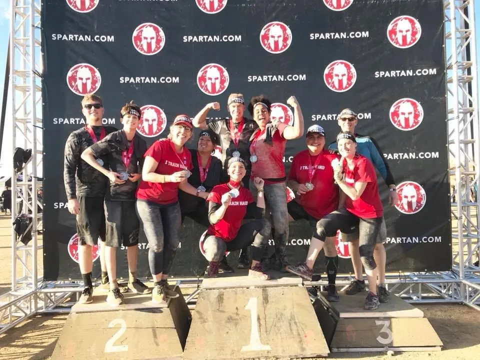 Action Fitness members in red shirts celebrating together on a Spartan race podium