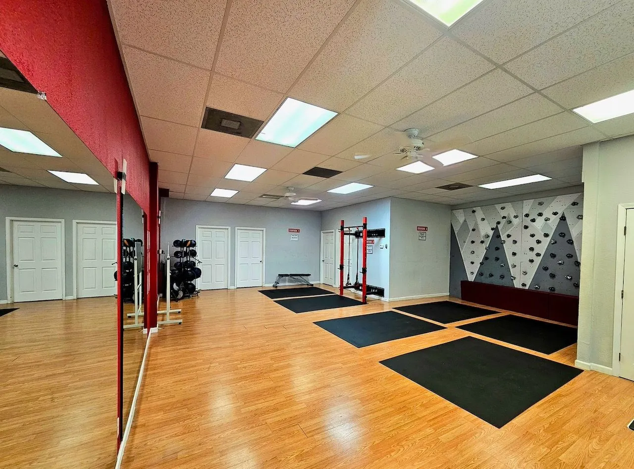 The open studio floor with wood flooring, mats, the squat rack and the climbing wall