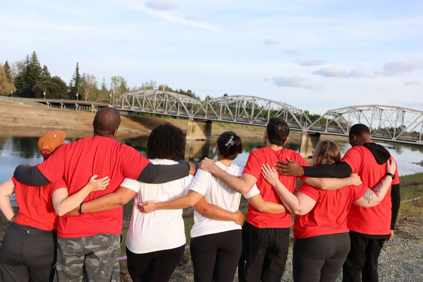 The Action Fitness crew in red shirts standing arm in arm by the river in Sacramento
