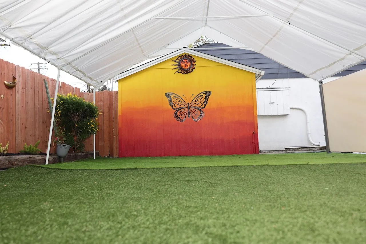 The outdoor turf area under a white canopy with a butterfly mural on the back wall