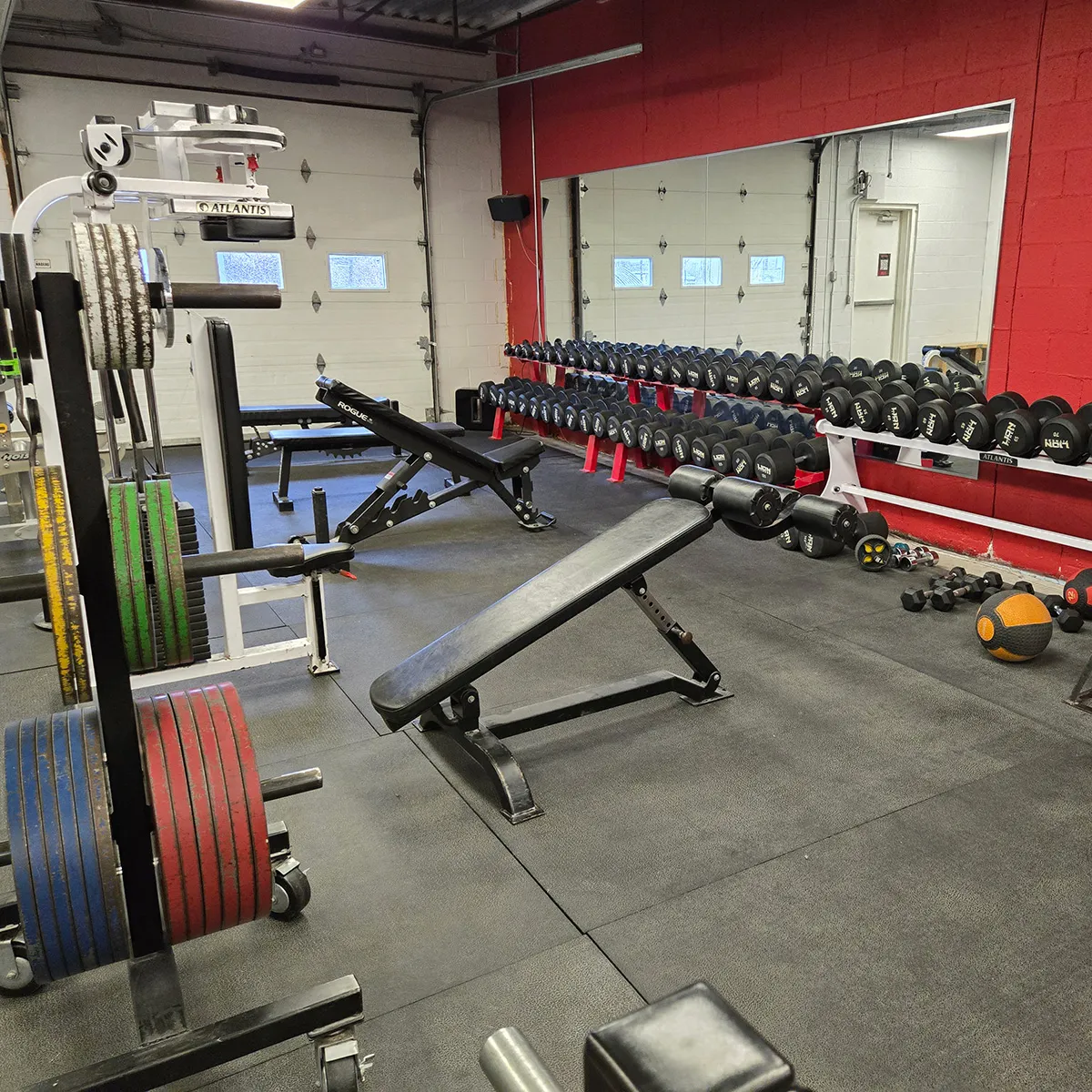A full rack of dumbbells against a red wall