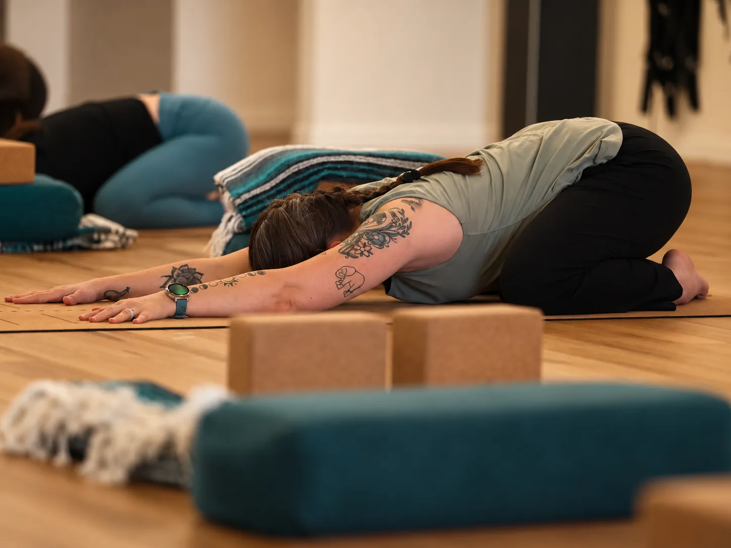 Students resting in child's pose over teal bolsters and cork blocks