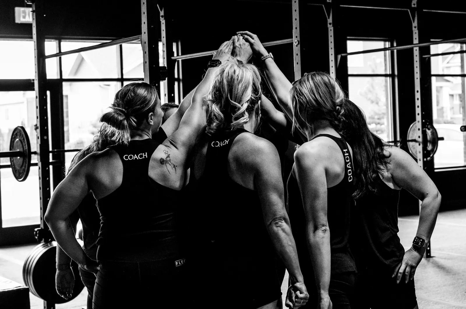 Coaches and members in a huddle with their arms raised, one wearing a coach shirt