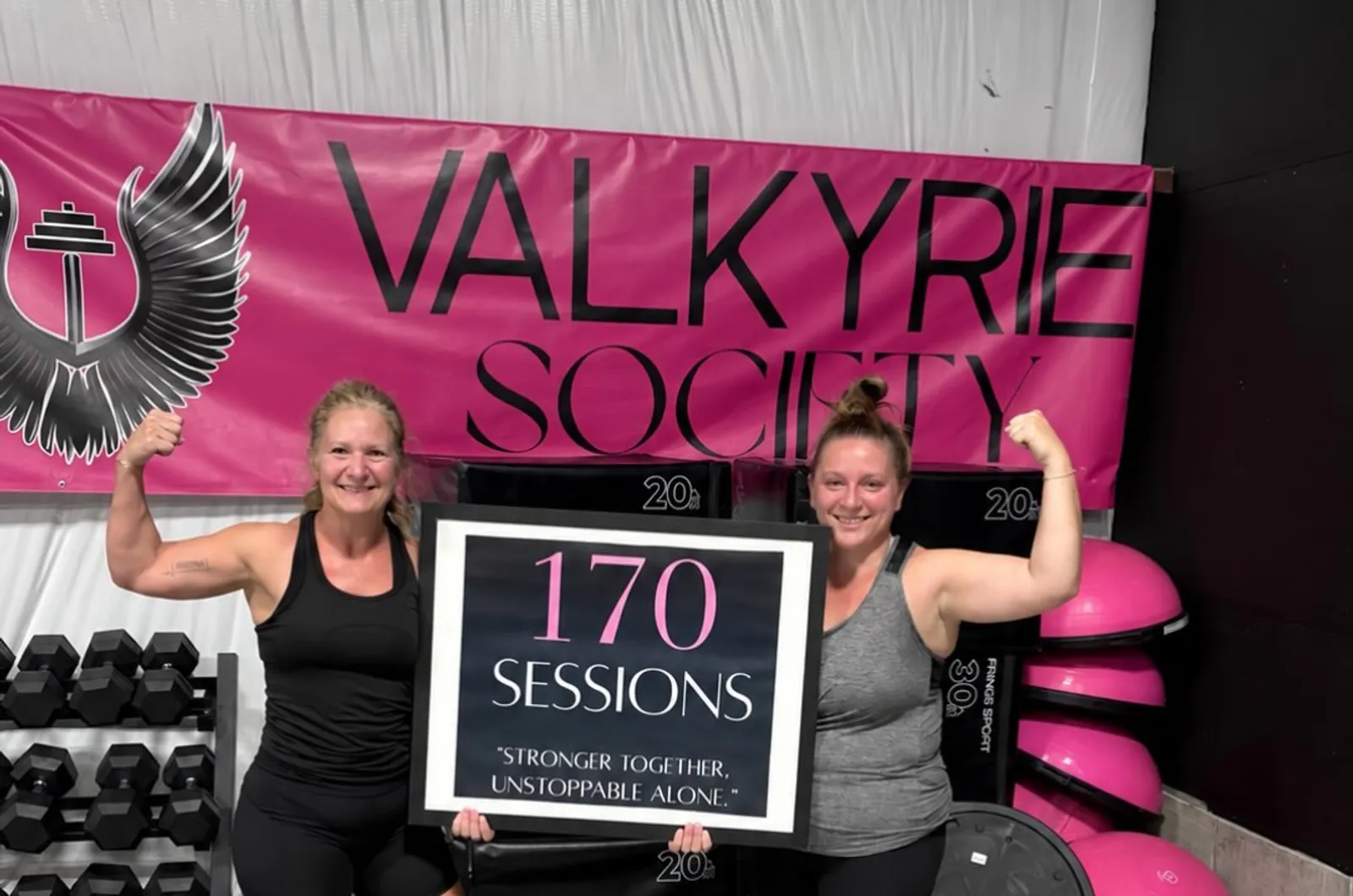 Two members flexing under the pink Valkyrie Society banner, holding a 170 sessions milestone sign