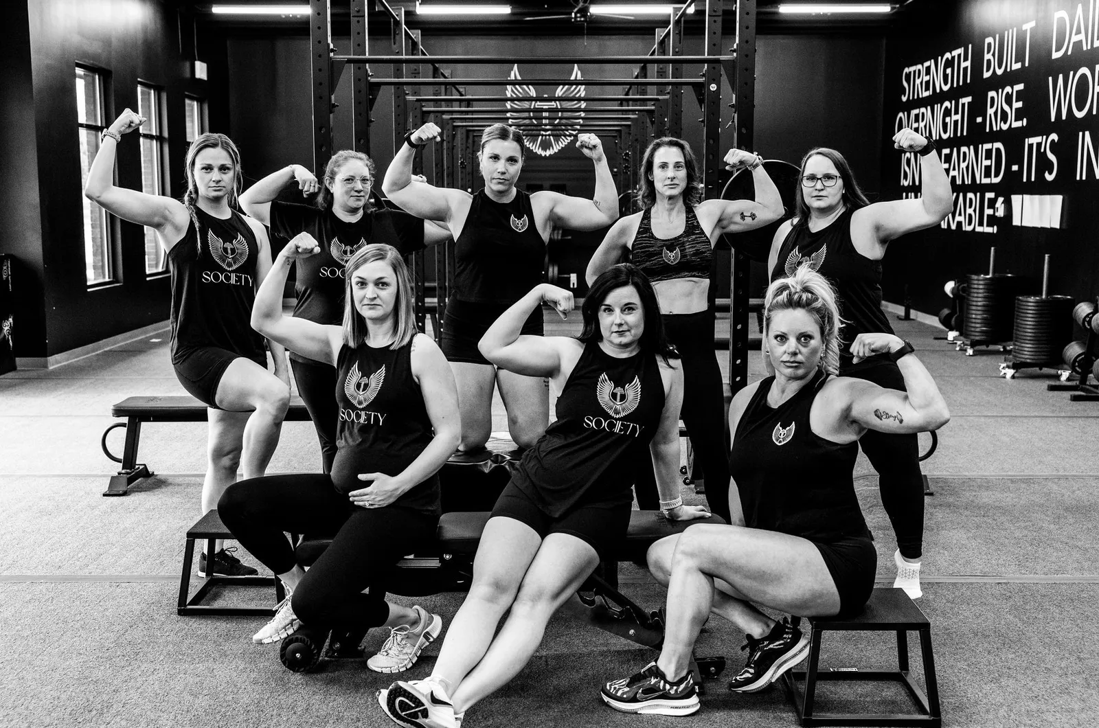 Ten members flexing together under the Strength Built Daily wall, in black and white